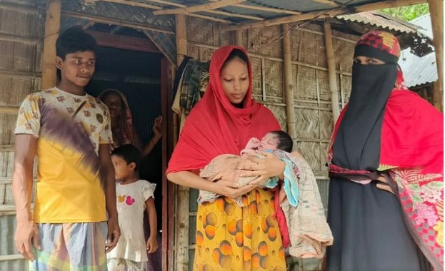 বদরগঞ্জ উপজেলার কুতুবপুরে নিজ বাড়িতে নবজাতককে কোলে নিয়ে দাঁড়িয়ে আছে মা মমতা বেগম